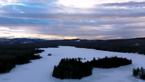 Luftaufnahmen,-Die-Bei-Sonnenuntergang-Rückwärts-Von-Einer-Mit-Kiefern-Bedeckten-Insel-Inmitten-Eines-Zugefrorenen-Sees-Fliegen