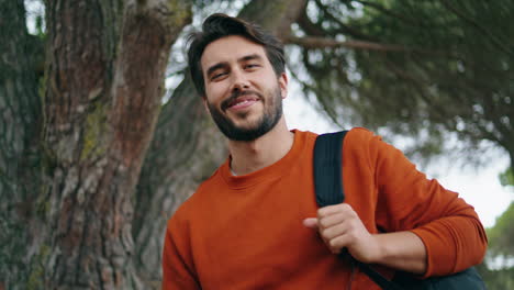 hombre barbudo y guapo retrato vertical sonriendo en el parque. hombre sosteniendo una mochila