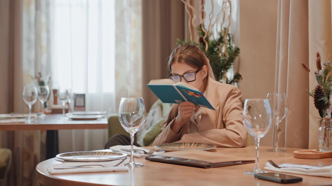 Afslappende café-læsning. Rolig kaffebar-indstilling med læsende kvinde og frodigt grønt. Behagelig caféscene, der viser kvinde fordybet i sin bog midt i rolig indretning og blødt sollys