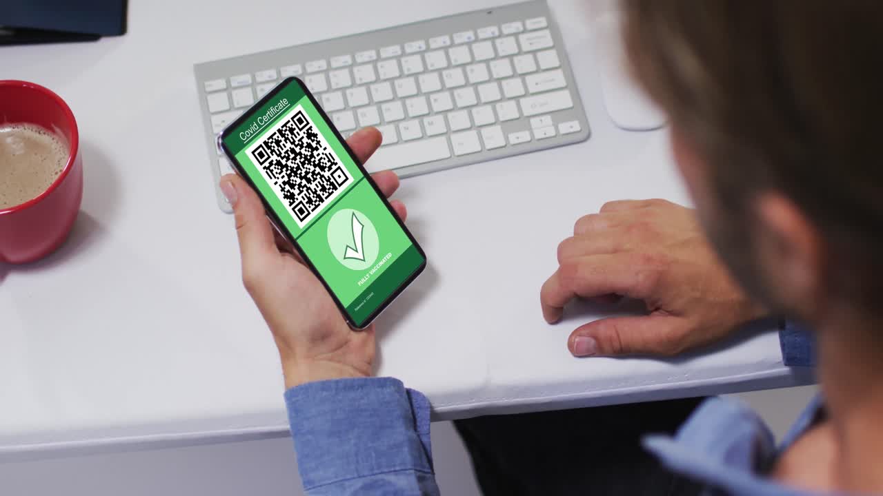 hombre en el escritorio sosteniendo un teléfono inteligente con certificado de vacunación contra la covid y código qr en la pantalla