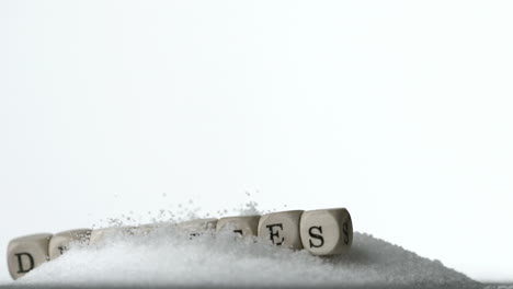 dice spelling out diabetes falling over pile of sugar on white background