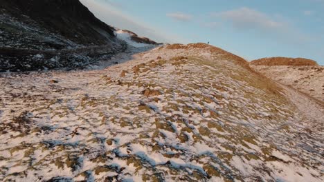 Vista-De-Cerca-De-La-Nieve-En-El-Acantilado-Rocoso-En-Islandia-Con-Un-Hombre-Con-Gafas-Vr-Parado-En-La-Cima-En-Un-Día-Soleado---Disparo-De-Drones