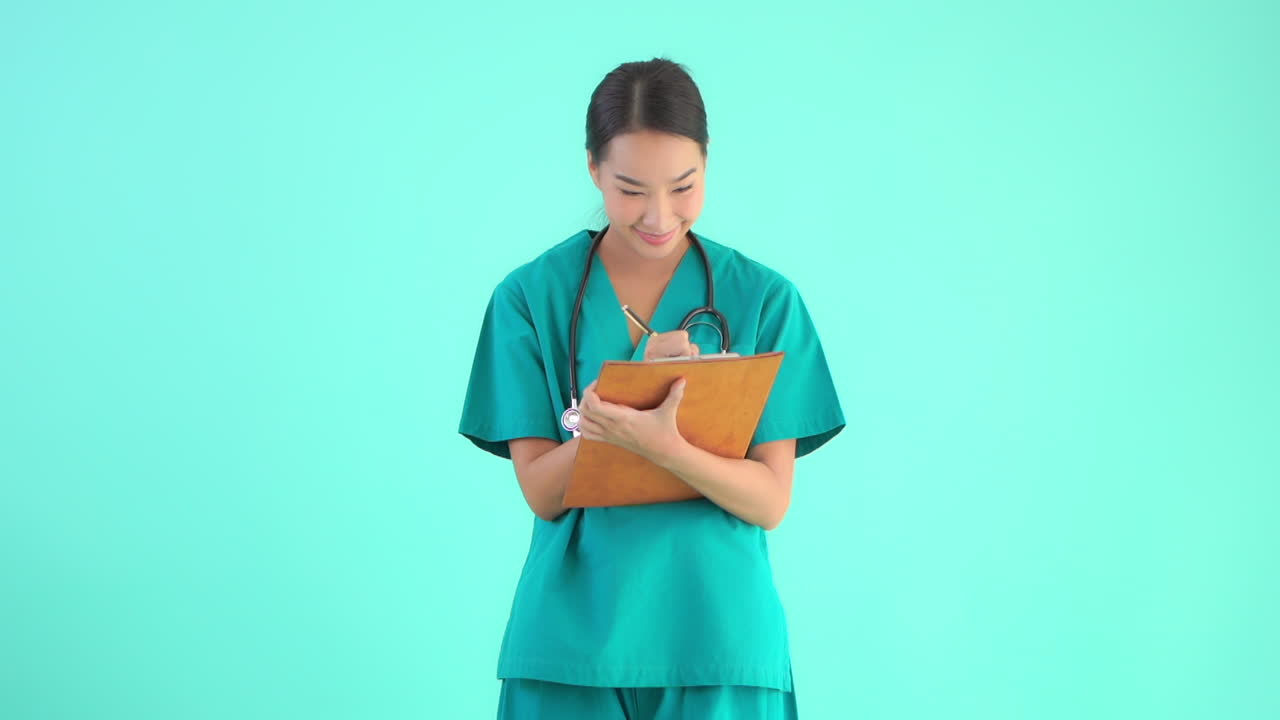 청록색 스튜디오 배경에서 목에 청진기를 걸고 클립보드에 메모를 하는 아시아 여성 외과 종양 전문의
