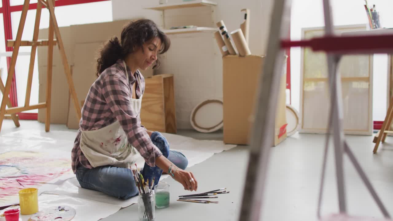 video de una artista femenina biracial pintando en el suelo en un estudio