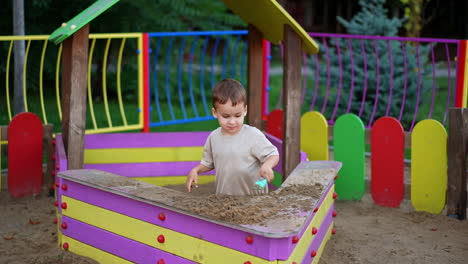cute caucasian toddler standing in the sandbox. happy kid playing with sand at the playground.