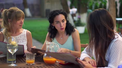 three pretty girlfriends talking and reading menu in cafe outdoors in the park