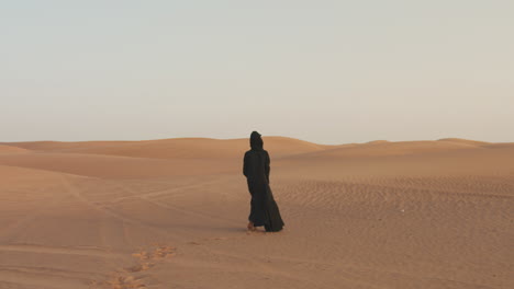 back view of a muslim woman with hijab walking barefoot in the desert