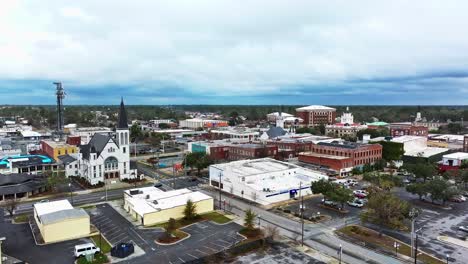 Cars on junction of Valdosta Town in Georgia during cloudy day. Red brick Buildings in downtown and white church., Aerial establishing wide shot.