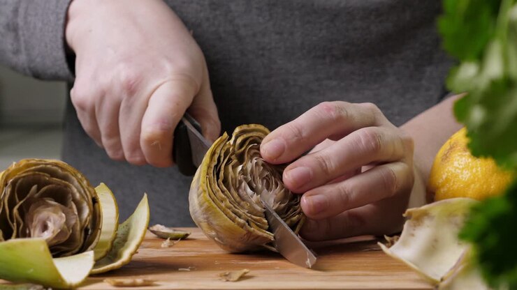 Woman cleaning artichokes with knife. Cooking process at the kitchen. Closeup