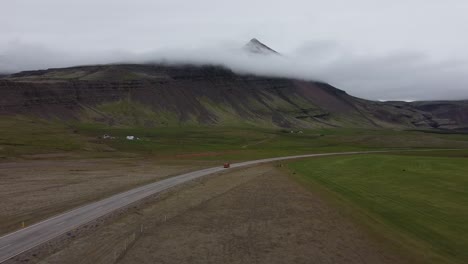 red car travels on empty road in iceland countryside with mountain backdrop, drone view