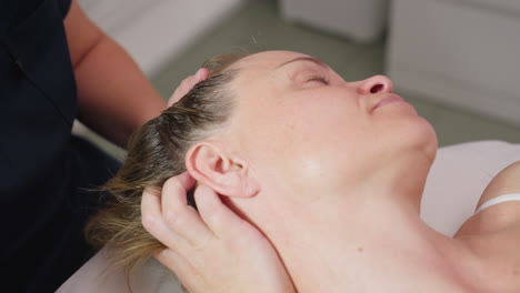 beauty expert gliding fingertips from neck to head over relaxed female client in serene spa, close up reveals gentle massage technique promoting calm atmosphere for stress relief and rejuvenation