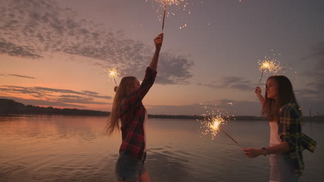 un grupo de amigas, chicas y hombres bailan en la playa con chispas en cámara lenta al atardecer. celebran el año nuevo en la playa