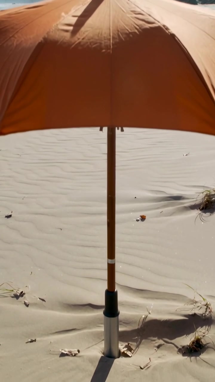 Video verticale: Movimento all'indietro della telecamera che rivela un ombrellone arancione sulla sabbia per mostrare il palo in legno e la custodia.