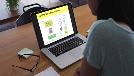 Woman-working-at-desk,-covid-vaccination-certificate-with-qr-code-on-laptop-screen