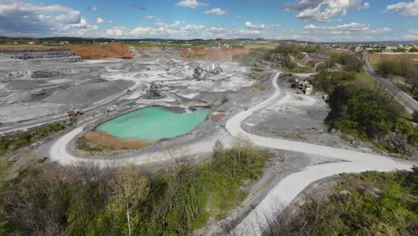 Drone-view-of-a-Quarry-with-a-small-lake,-heavy-industry-and-loading-trucks-on-sight