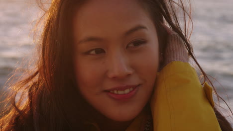 Porträt-Einer-Glücklichen-Asiatischen-Frau,-Die-Lächelt-Und-Den-Urlaub-Genießt,-Den-Reiselebensstil-Erkundet,-Sich-Am-Strand-Entspannt-Und-Sich-Bei-Sonnenuntergang-Mit-Windigen-Haaren-Positiv-Fühlt