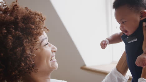 mother playing game with newborn baby son and lifting him in air in loft apartment