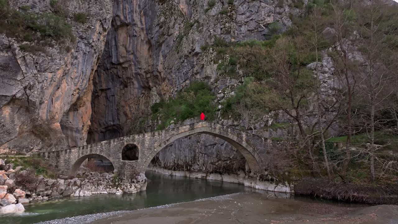 Antik köprüde huzurlu bir vadiye bakan adamın drone görüntüsü.
