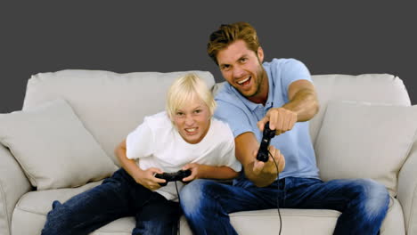 father and son playing video games on the sofa on grey background