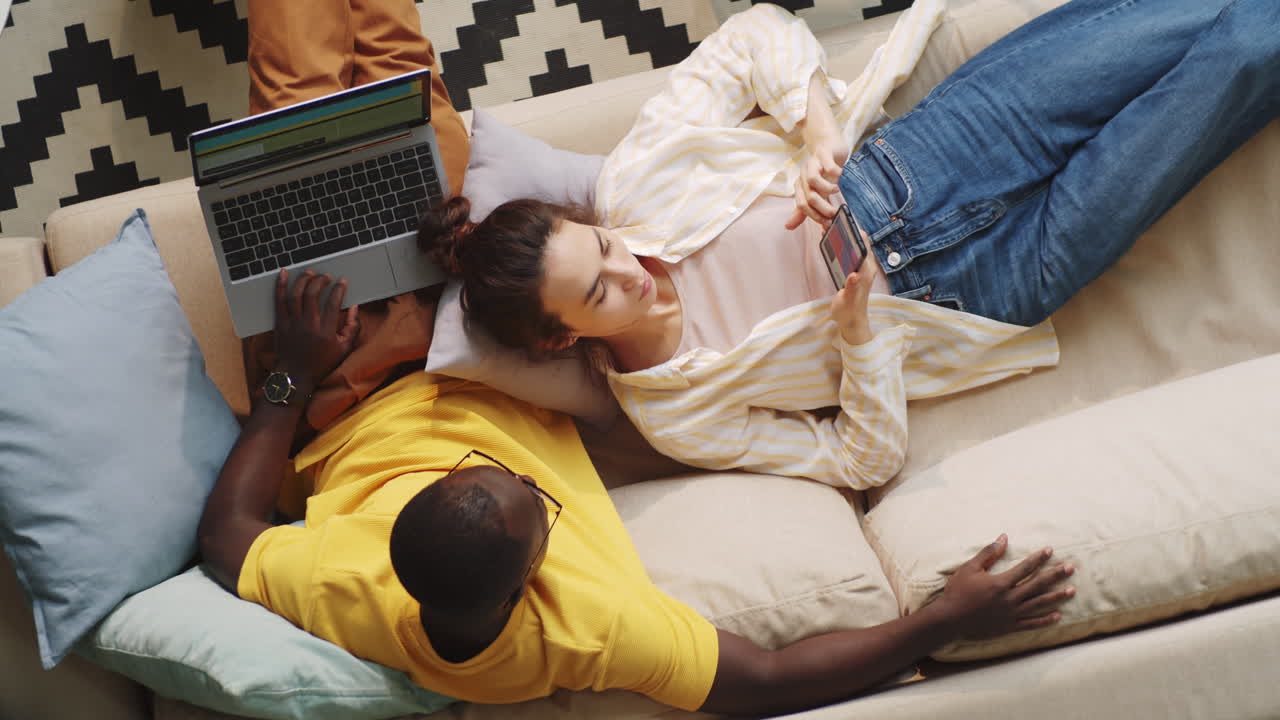 Diverse Couple Using Laptop and Smartphone on Sofa