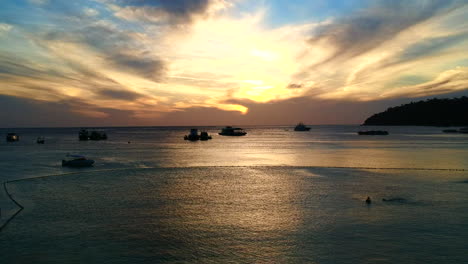 An-aerial,-beautiful-colour-wide-shot-of-an-ocean-while-sun-is-setting-with-boats-and-waves-on-the-foreground