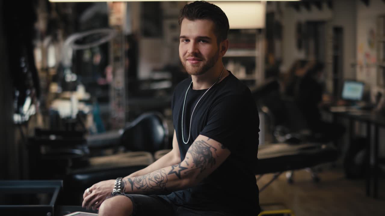 디지털 태블릿에서 모티브를 디자인하고 카메라를 보는 백인 문신 예술가의 초상화.