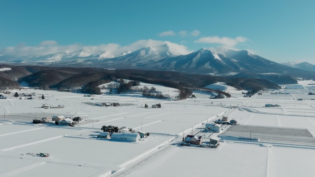 Snow-blanketed Farmlands In Nakafurano, Hokkaido, With The Mountain Range In Background. wide aerial shot