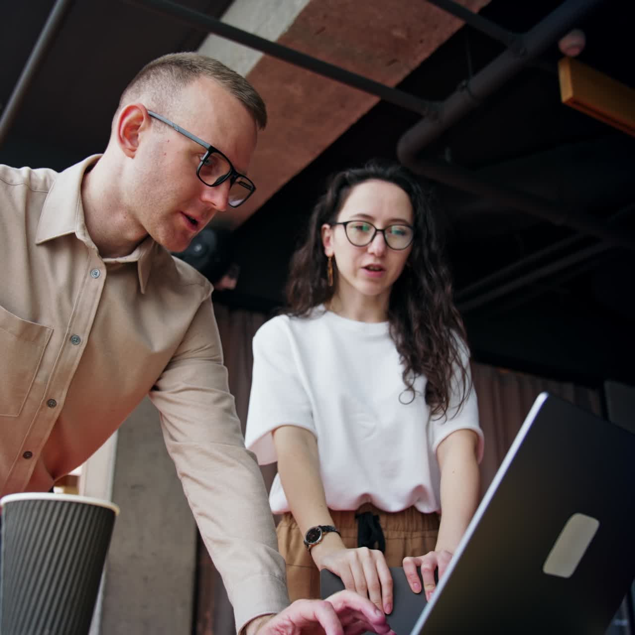 Productive communication between the colleagues in office. Coworkers are focused on laptop screen discussing what they see. Low angle view