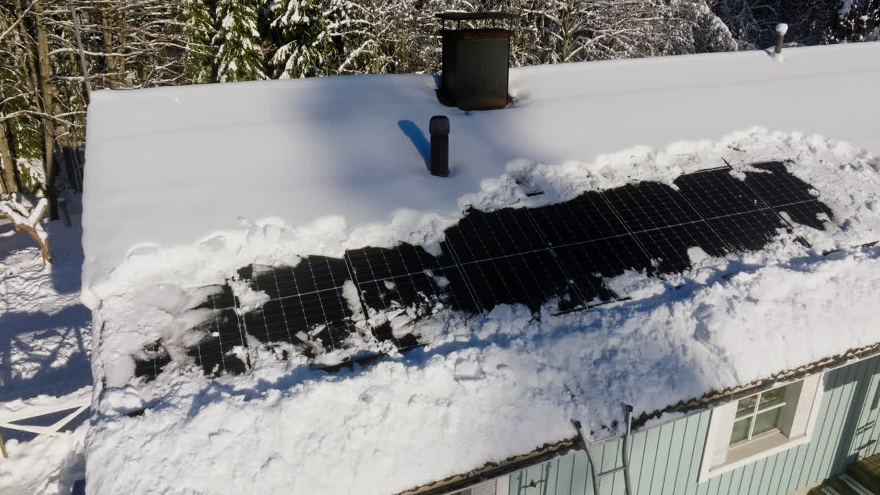 vista aérea de un techo de casa con celdas solares parcialmente limpiadas y nevadas, un día soleado de invierno