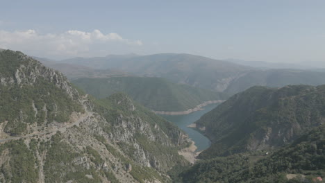 drone shot flying over the mountains near the koman lake in albania on a sunny day with clouds with blue water and a green valley log