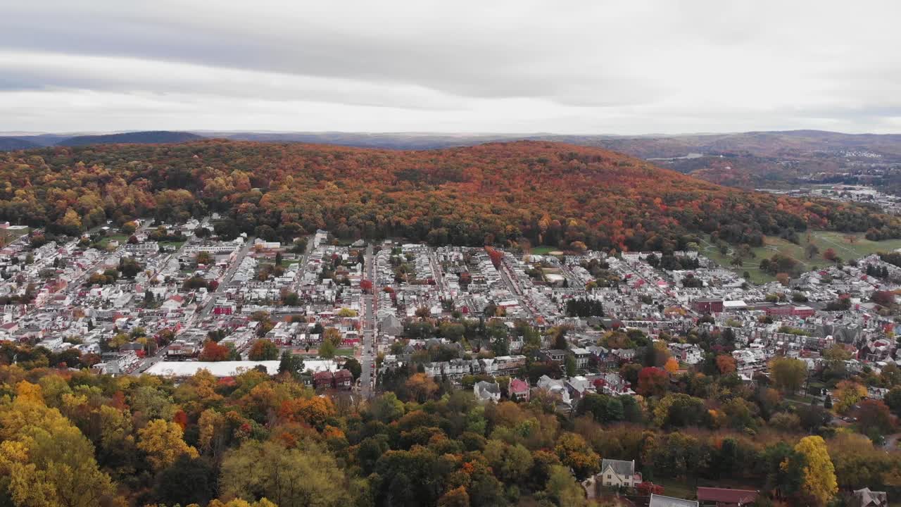 leyendo el paisaje urbano intercalado entre el colorido paisaje del bosque otoñal, pennsylvania, estados unidos, dolly en antena