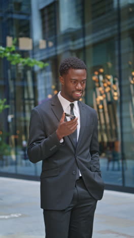 vertical video shot of young businessman wearing suit talking on mobile phone using built in microphone standing outside offices in the financial district of the city of london uk shot in real time