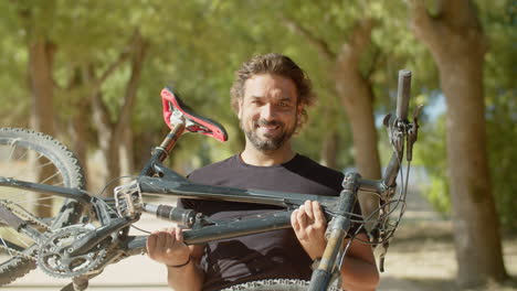 front view of happy bearded man lifting his bike after workout