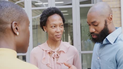 three happy african american male and female colleagues talking outside building, in slow motion