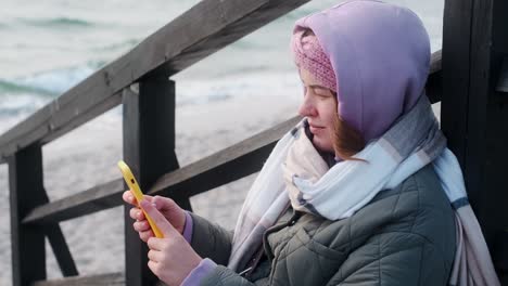 woman using phone at the seaside in winter