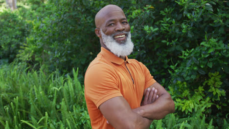 portrait of african american senior man smiling and crossing his arms in the garden