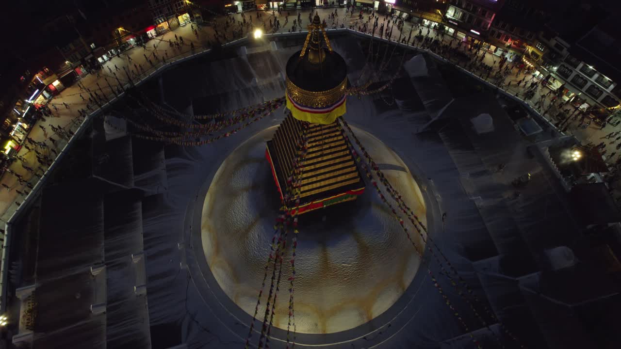A serene night drone view of Boudhanath Stupa, also known as boudha nath, glowing above Kathmandu. The sacred Buddhist landmark stands radiant against the quiet urban nightscape