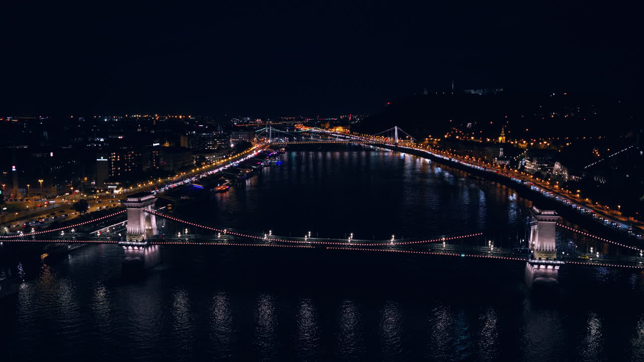 Flying On The Chain Bridge Budapest At Night Over The River Danube In Hungary. Aerial Drone Shot