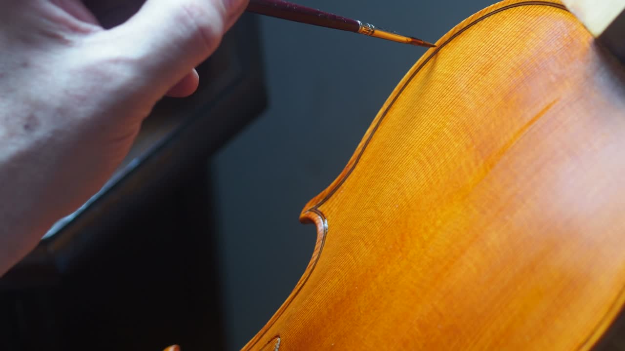 mano de un luthier fabricante de violines barnizando un instrumento de cuerda de madera hecho a mano