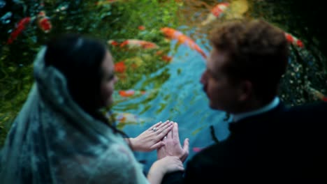 couple holding hands by a koi pond