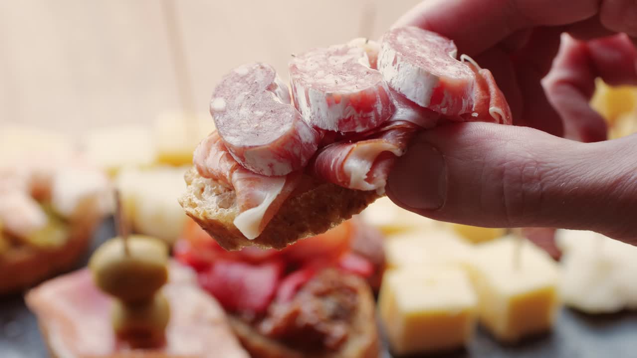 Hand holding a tapas plate with sausage and ham