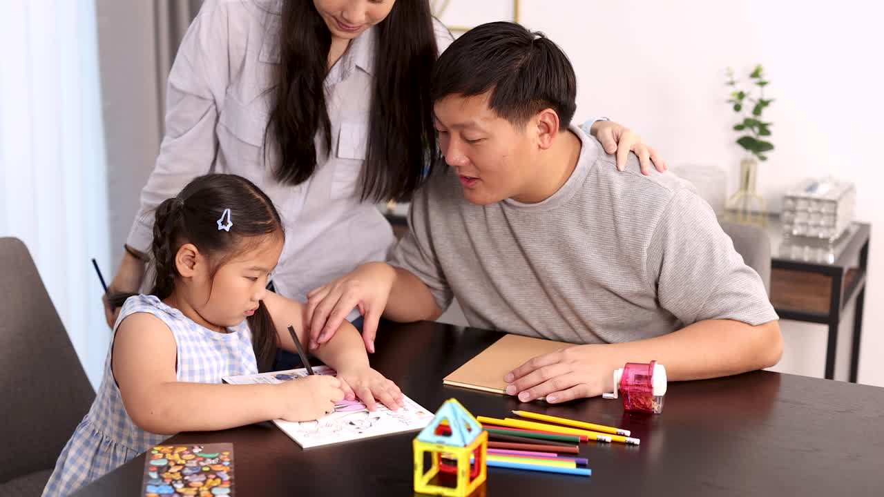 Parents assist daughter with drawing and learning activities in bright, cozy home environment, static camera