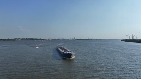 tanker ship sailing through the river, wind farm at background, aerial view