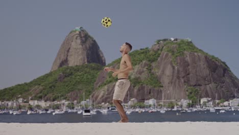 man juggling soccer ball on rio de janeiro beach with sugarloaf mountain