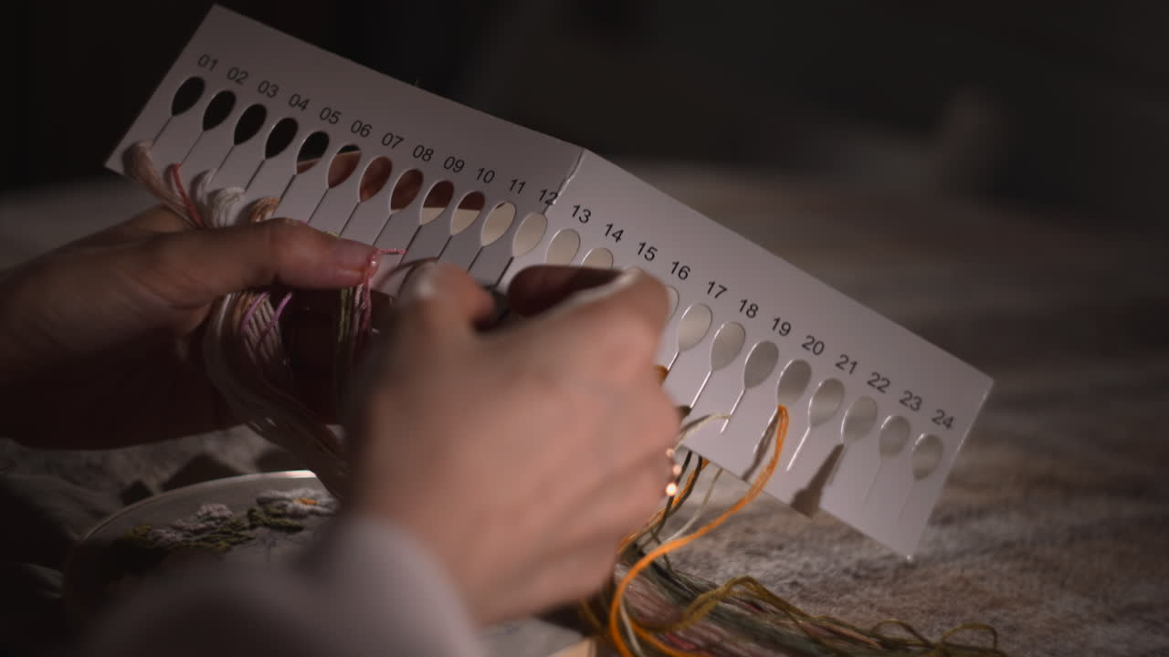 Hvid kvinde vælger brodergarn fra nummereret farvekort, nærbillede af hænder der sorterer tråde, nummererede farveprøver