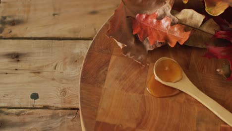 video of maple syrup on wooden spoon and board with autumn leaves