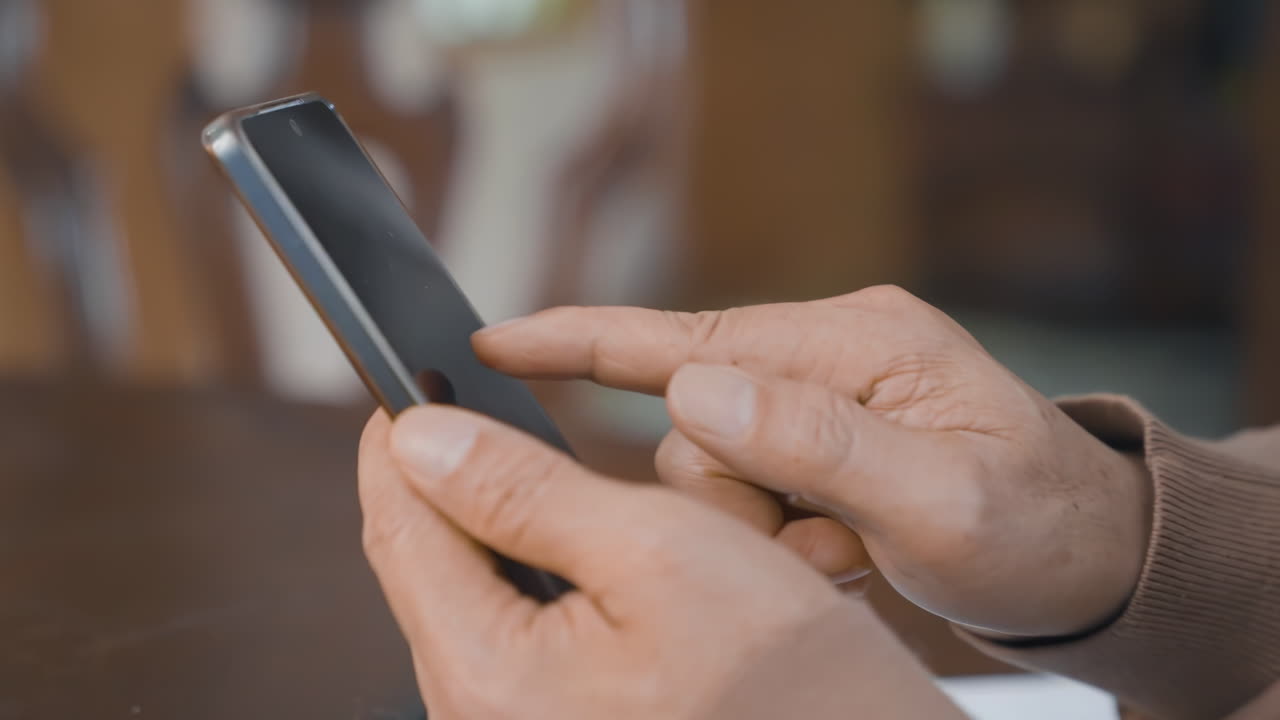Anziano pensionato che utilizza lo smartphone seduto sul divano di casa, naviga su siti web, guarda video online, usa app di messaggistica digitale, fa acquisti online e scorre i social media.