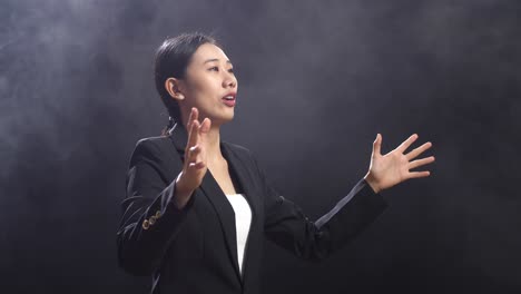 side view of asian speaker woman in business suit holding her hands together while speaking in the black screen studio