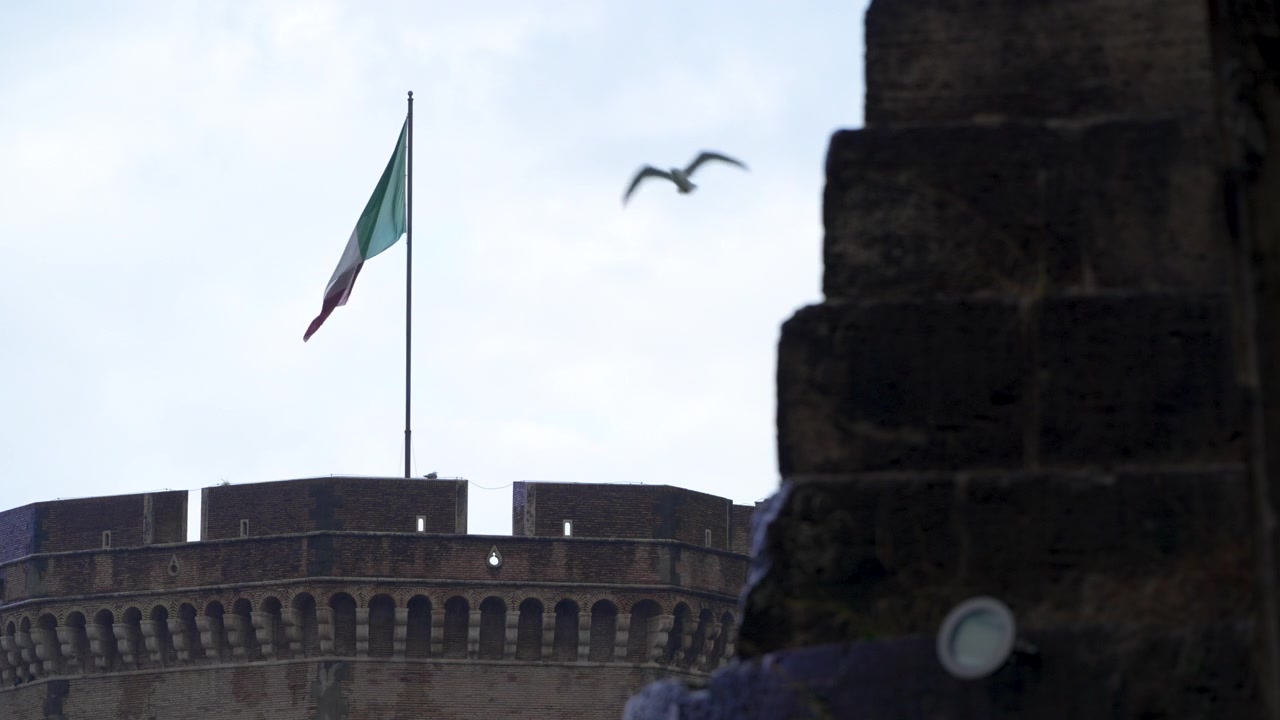 Bandiera italiana che sventola sopra la torre rotonda di Castel Sant'Angelo, incorniciata da pietra scura sotto una luce soffusa e nuvolosa