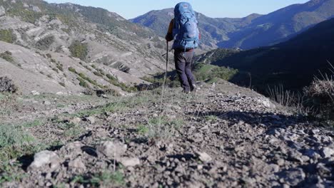 Hiker-walks-with-heavy-backpack-and-poles-in-remote-mountain-landscape
